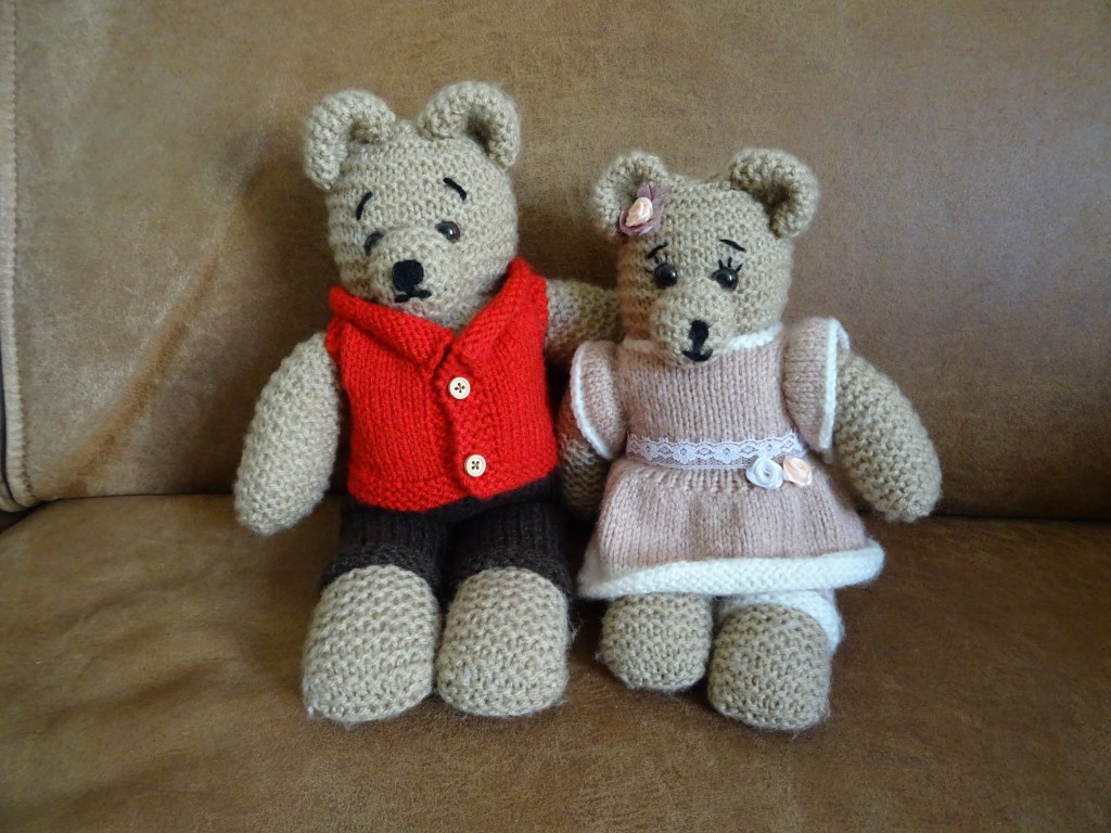Twee gebreide knuffelberen. De één met een jurkje aan en de ander met een jasje en een broek.