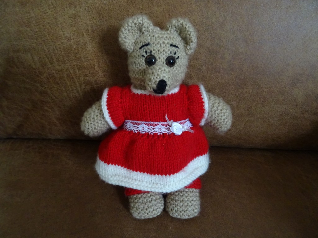 Gebreide knuffelbeer met een rood-wit jurkje en daaronder een rood-witte legging.